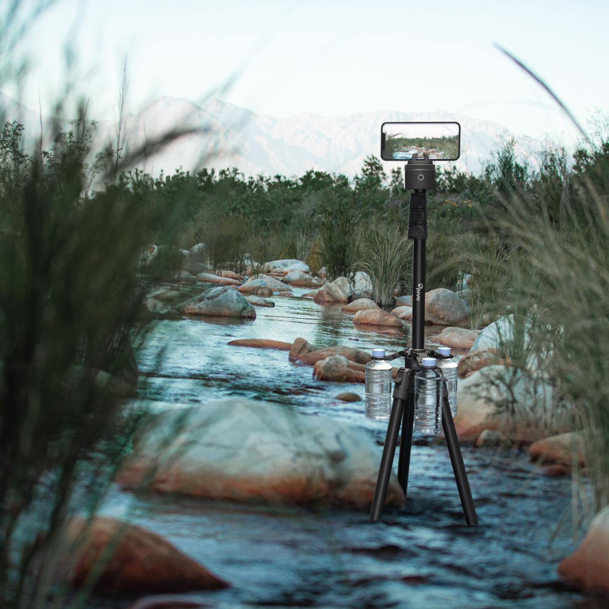 Pivo Tripod Weight stabilizing a tripod with water bottles by a scenic river.