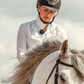 Person wearing a compact wireless Bluetooth mic clipped to shirt while riding a white horse outdoors