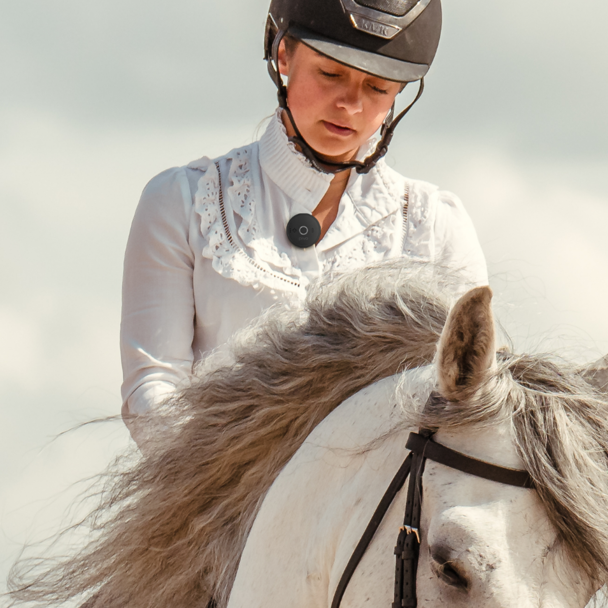 Person wearing a compact wireless Bluetooth mic clipped to shirt while riding a white horse outdoors